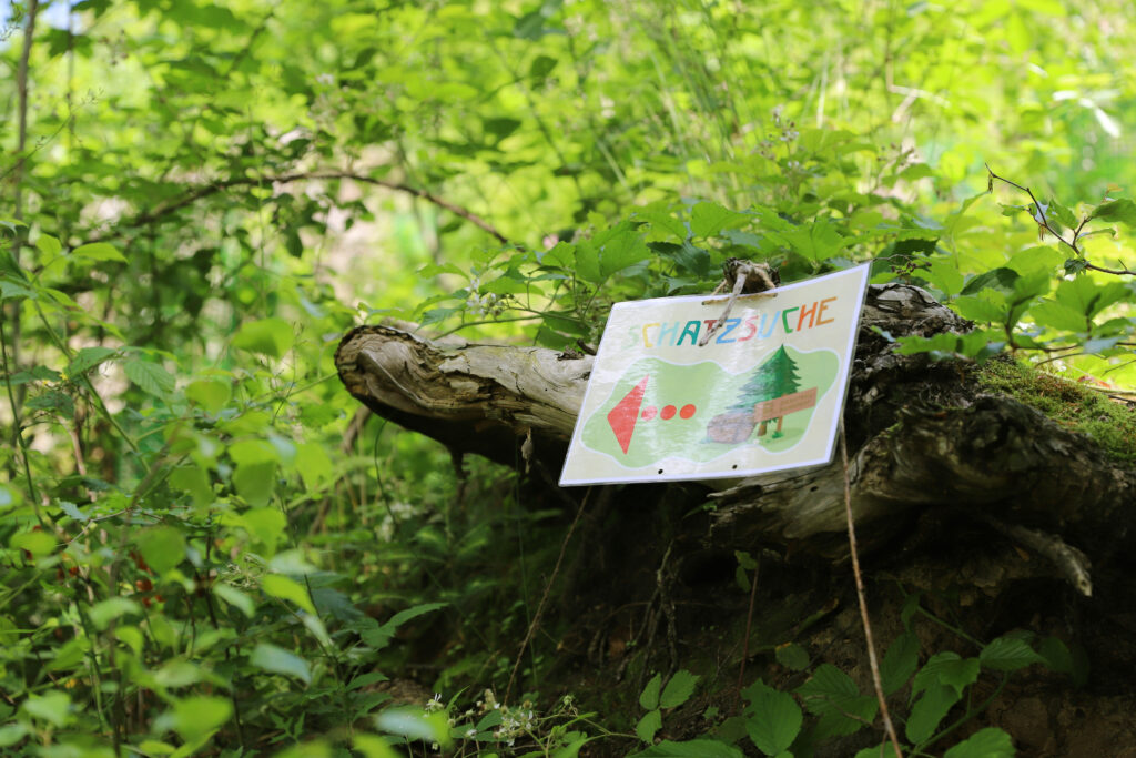 Hinweisschild zur Schatzsuche hängt im Wald an einem Baumstamm