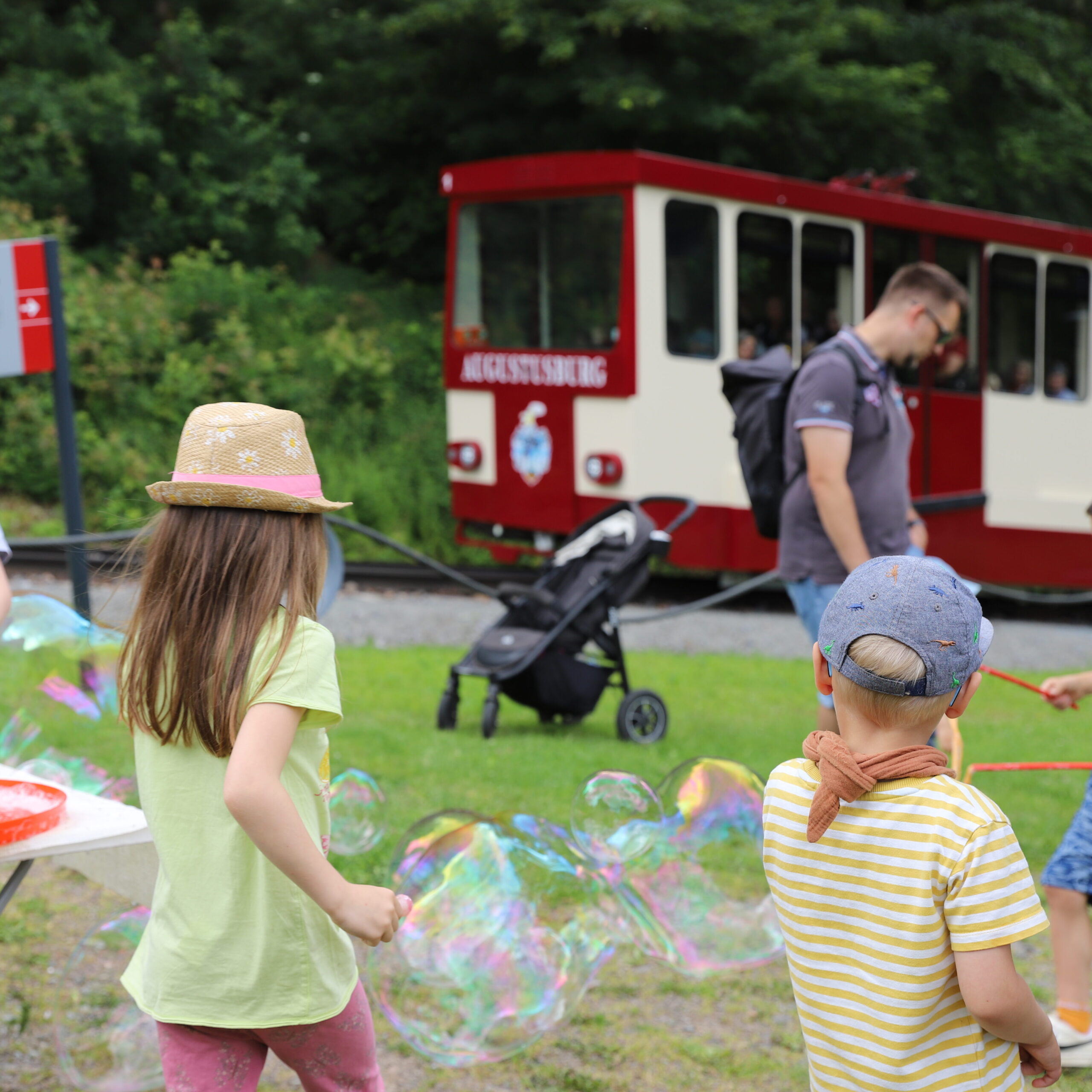 Kinder spielen mit Seifenblasen, im Hintergrund die Drahtseilbahn